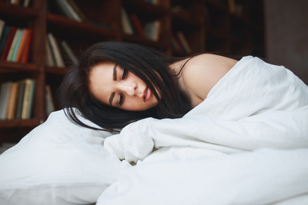 Sensual woman with dark hair lying on a bed at homeの写真素材
