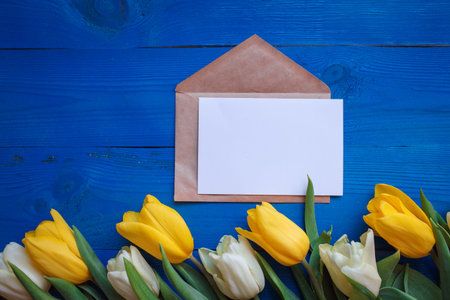 Spring tulip flowers, gift paper card on blue wooden table from above in flat lay style. Greeting...