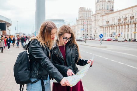Two young stylish women traveling and looking at the map in cityの写真素材
