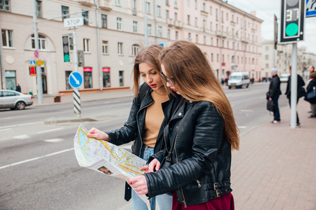 Two young stylish women traveling and looking at the map in cityの写真素材