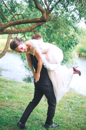 Portrait of a handsome young man carrying attractive woman on his back outdoors . Fun couple. Bride and groomの写真素材