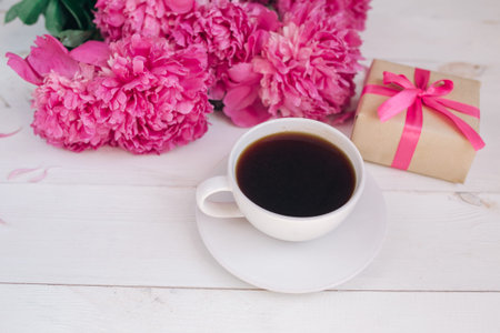 A cup of coffee, pink peonies pattern and gift box on white wooden backgroundの写真素材