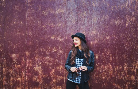 Young stylish woman in a city street. beautiful brunette girl walking around the city.leather jacket,urban backpack , bright red lips and hatの写真素材