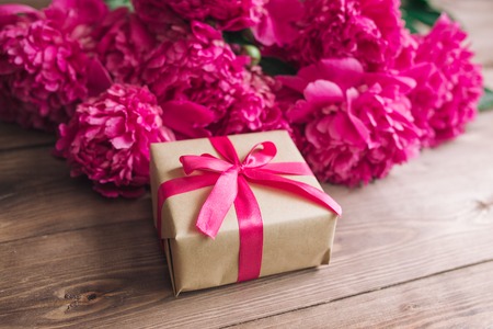 Row of peonies and gift box on wooden background with space for message. Women's or Mother's Day background. Top viewの写真素材
