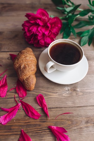 A cup of coffee , red peonies pattern and croissant on wooden background . Good morning .Women's or Mother's Day background. Top viewの写真素材