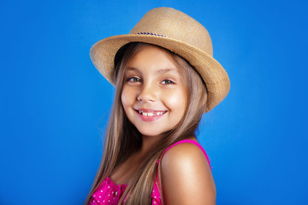 Portrait of young cute girl in pink dress and hat on blue background .Summer vacation and travel...