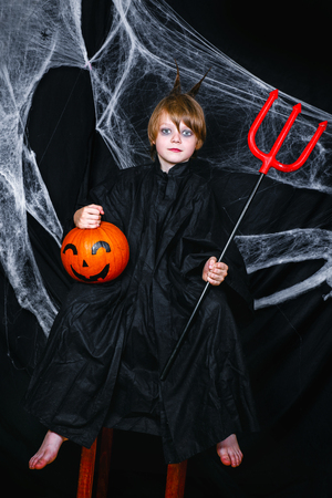 Cute little boy sitting on the pumpkin on black background with a cobwebの写真素材