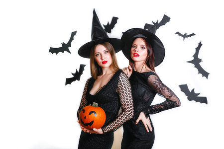 Two happy women in black witch halloween costumes with pumpkin on party over white backgroundの写真素材