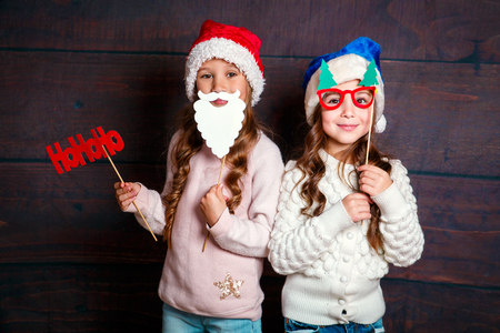Two little smiling girls having fun .Christmas concept. Smiling funny sisters in Santa hat on wooden backgroundの写真素材