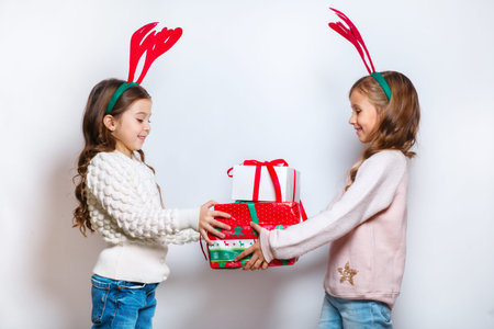 Two happy little smiling girls with christmas gift boxs..Christmas concept. Smiling funny sisters in deer horns in studio.の写真素材