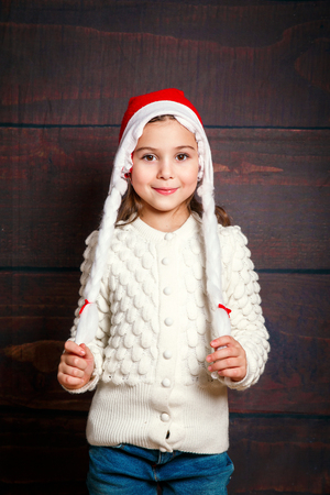 Happy little smiling girl .Christmas concept. Smiling pretty funny girl in Santa hat on wooden background.の写真素材