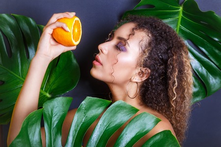 Close-up of beautiful girl posing in tropical forest. Portrait of beautiful African American woman with orangesの写真素材