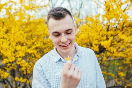 Happy smiling romantic young man with spring yellow flowers at gardenの写真素材