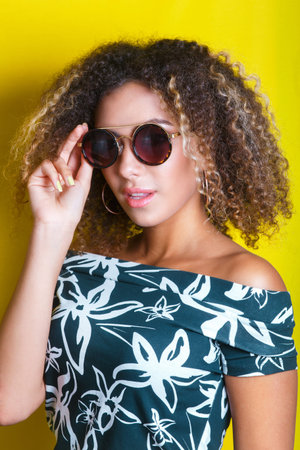 portrait indoors of a young afro american woman in sunglasses. Yellow background. Lifestyle.の写真素材