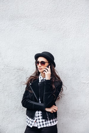 Smiling urban girl uses smart phone with smile on her face.Portrait of fashionable gir wearing a rock black style having fun outdoors in the cityの写真素材