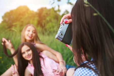 attractive pretty young woman talking pictures her friends in park in summerの写真素材
