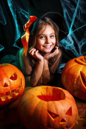 Happy halloween. Pretty little child girl in witch costume with carving pumpkin . Happy family preparing for Halloween.の写真素材