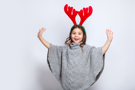 Happy little smiling girl showing product. Christmas concept. Smiling funny girl in deer horns on white backgroundの写真素材