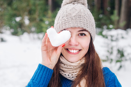 Young cute woman holding snow heart in winter forest. Love concept. Valentine day background.の写真素材