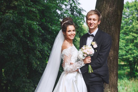 Beautiful wedding couple in park. Bride and groom hug each other outdoorの写真素材