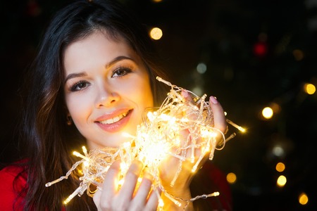 Beautiful young woman smiling and talking garlands of lights at homeの写真素材