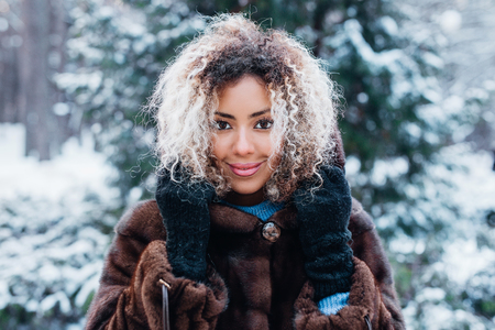 Close-up portrait of beautiful young afro american woman in snow winter forestの写真素材