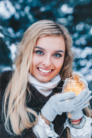 Christmas portrait of beautiful young girl in winter forest with lights outdoorの写真素材