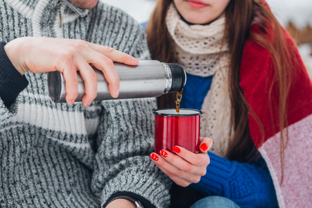 Young couple drinking hot tea on snowy sunny day in parkの写真素材