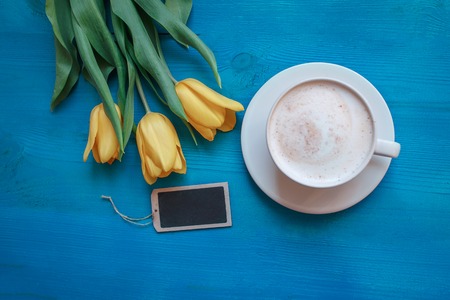 Coffee mug with yellow tulip flowers and notes on blue rustic table from above, breakfast on Mothers day or Womens dayの写真素材