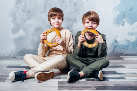 Two cute twin boys sitting on floor and happily eating healthy foodの写真素材