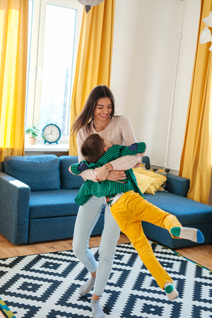 Beautiful woman and her cute little son are playing and smiling at homeの写真素材