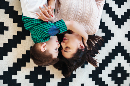 Top view of beautiful woman and her cute little son smiling while lying on the floor at homeの写真素材