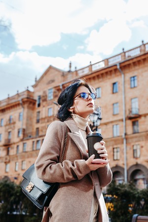 Beautiful elegant woman in sunglasses and coat with coffee in cityの写真素材