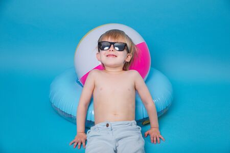 Little smiling boy in sunglasses with big inflatable ball on blue backgroundの写真素材