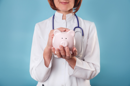 Medical professional holds piggy bank on blue backgroundの写真素材