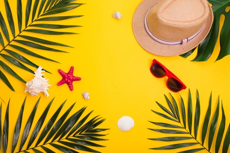 Hat,tropical palm leaves, sunglasses, sea shells on yellow background. Summer concept. Flat lay, copy spaceの写真素材