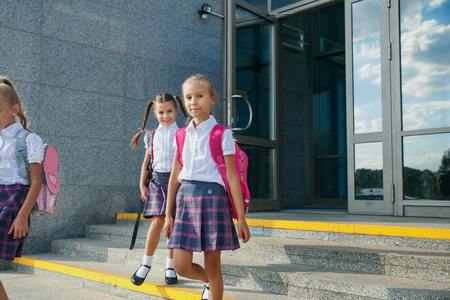 Group of elementary school kids running out of school buildings towards camera at the end of classの写真素材