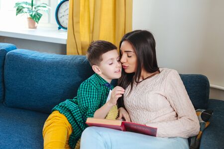 Young woman and her little child reading book at homeの写真素材