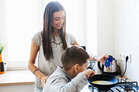 Happy mother with son cooking omelet in kitchen at homeの写真素材