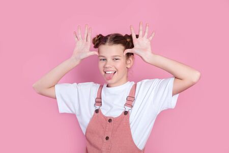 Funny girl grimacing with tongue out making ears protruding on pink backgroundの写真素材