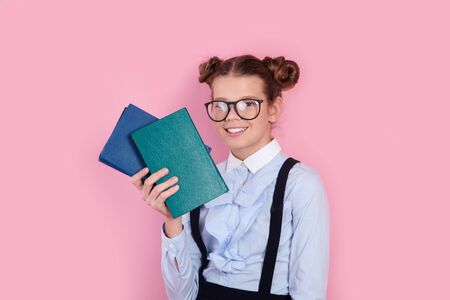 Young girl in school uniform and glasses holding books in her hands on pink studio backgroundの写真素材