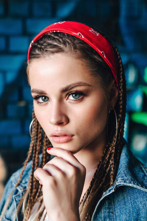 Fashion portrait of young hipster woman with bandana and braids on color wall