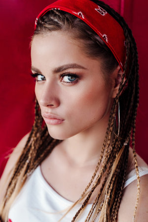 Fashion portrait of young hipster woman with bandana and braids on color city wall