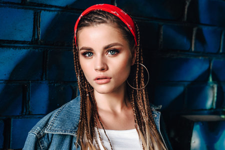 Fashion portrait of young hipster woman with bandana and braids on color wall