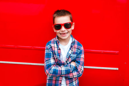 Portrait little boy wearing a checkered shirt and sunglasses in city over red backgroundの写真素材