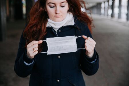 Scared woman holdng in hands in medical protective mask outdoorの写真素材