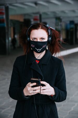 European woman with red hair in protective medical mask using smartphone in cityの写真素材