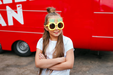 Little girl child wearing funny sunglasses standing in over city street backgroundの写真素材