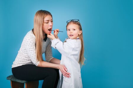 Adorable child dressed as doctor playing with mother indoor on blue backgroundの写真素材