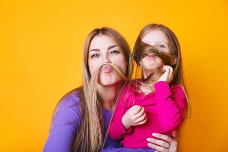 Close up photo amazing beautiful mom and small little daughter make moustache with curls pretend guy man on yellow backgroundの写真素材